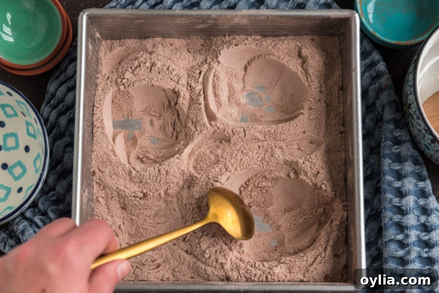 Creating three separate wells in the dry wacky cake mix using a spoon.
