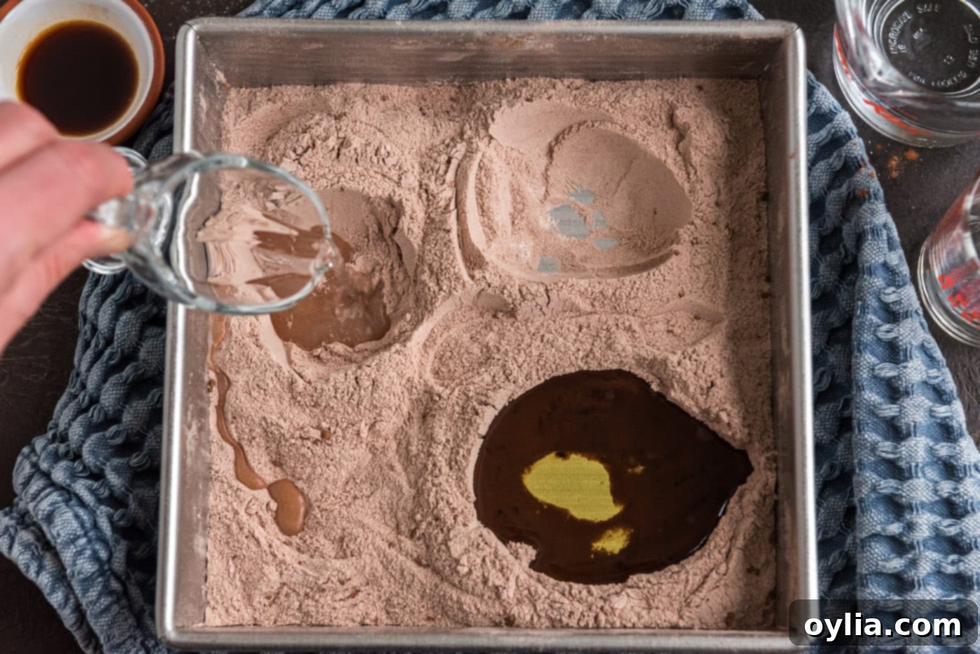 Pouring white vinegar into one of the smaller wells in the wacky cake dry mixture.