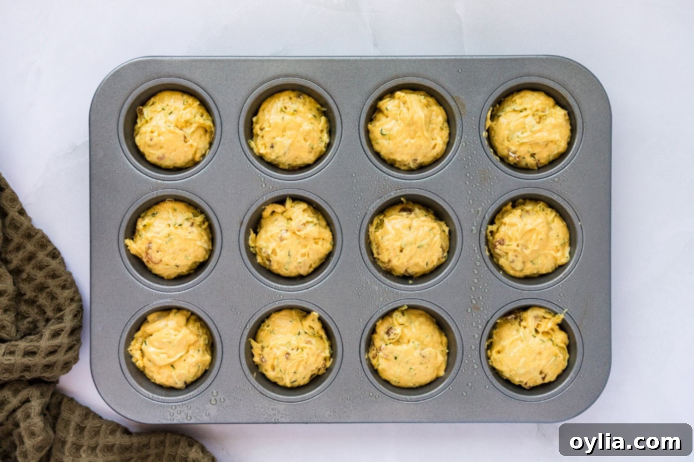 Muffin pan filled with zucchini muffin batter, ready for baking