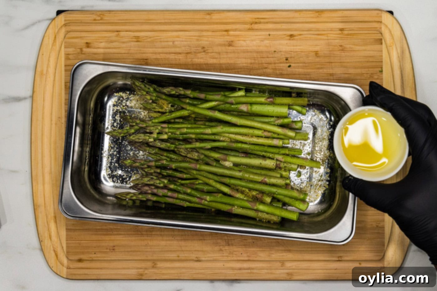 hand holding olive oil in a bowl over asparagus