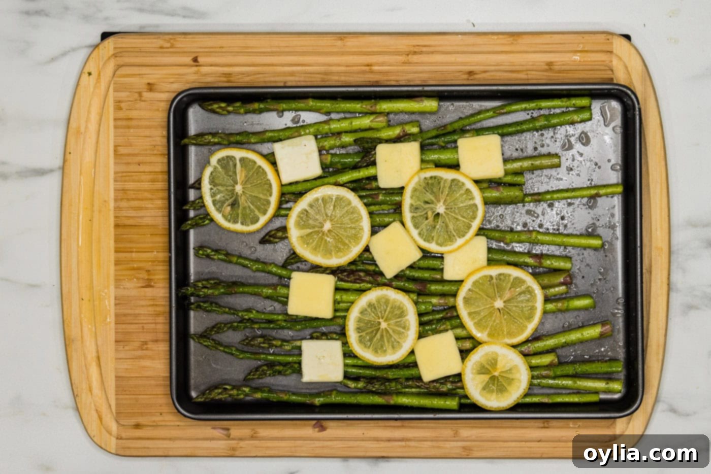 asparagus on a pan with butter pats and lemon slices