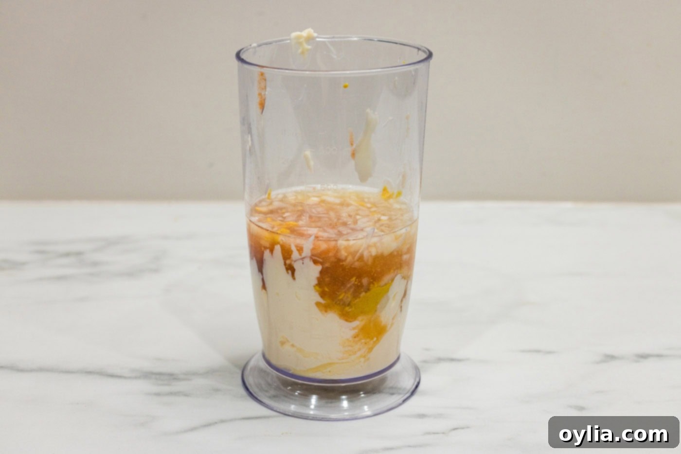 All essential remoulade sauce ingredients, including mayonnaise, mustards, horseradish, hot sauce, lemon juice, shallots, and garlic, are carefully added into a tall container, ready for blending.