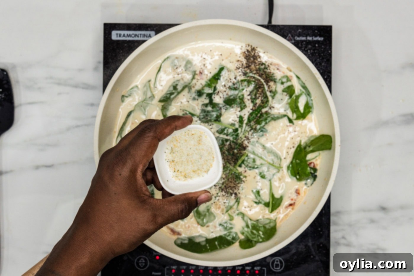 Fresh spinach leaves and garlic salt added to the creamy sauce in a skillet, about to wilt.