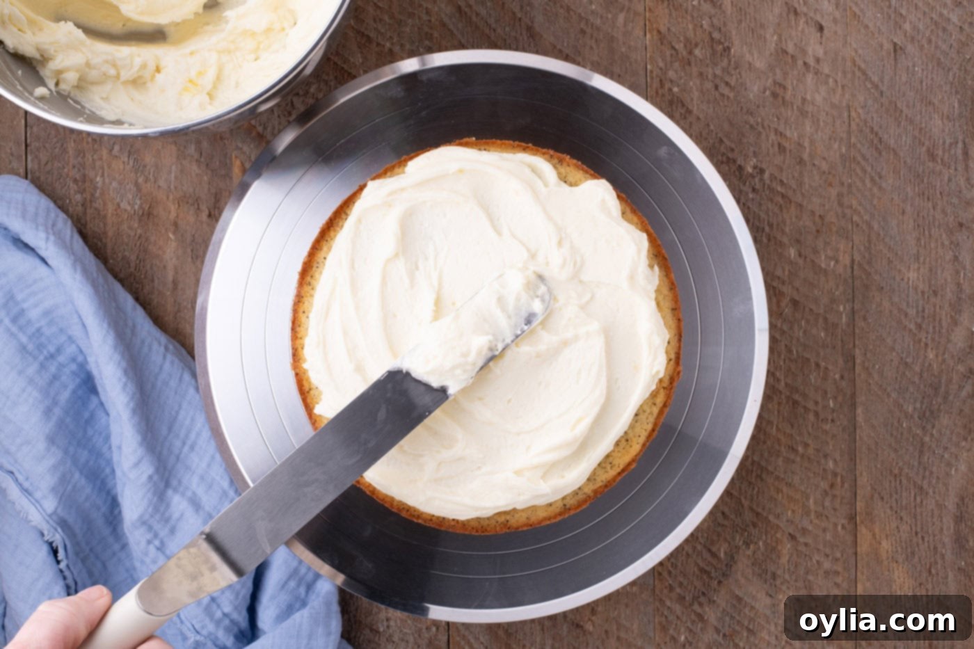 Icing spatula spreading lemon cream cheese frosting on a cake layer