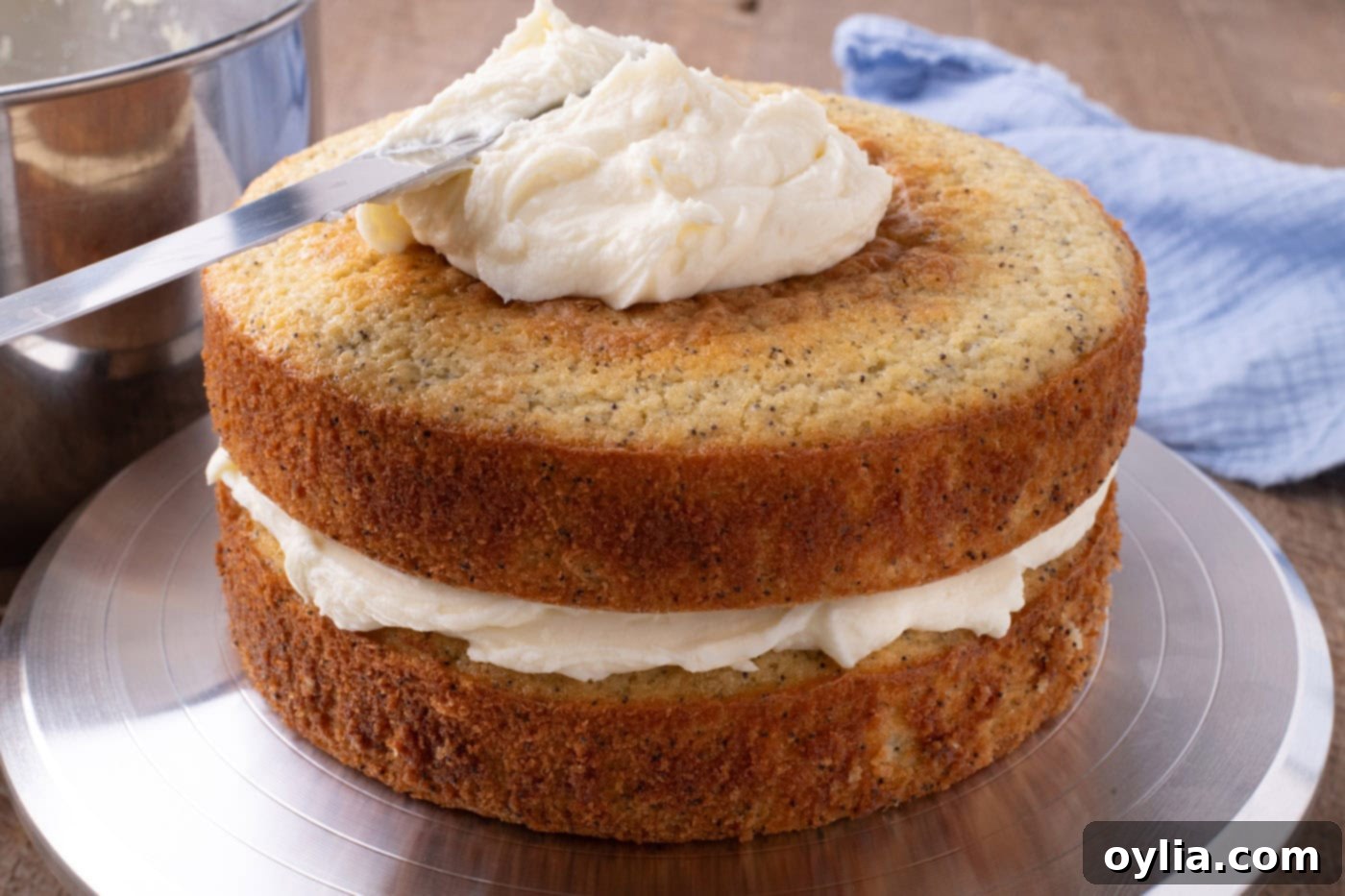 Spreading a thin crumb coat of lemon cream cheese frosting over stacked cake rounds