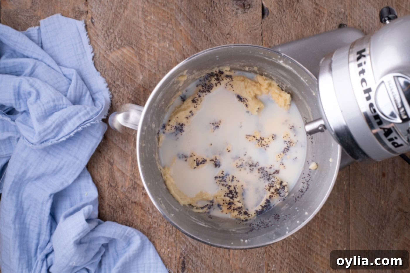 Poppy seeds and buttermilk being added to lemon cake batter in a stand mixer