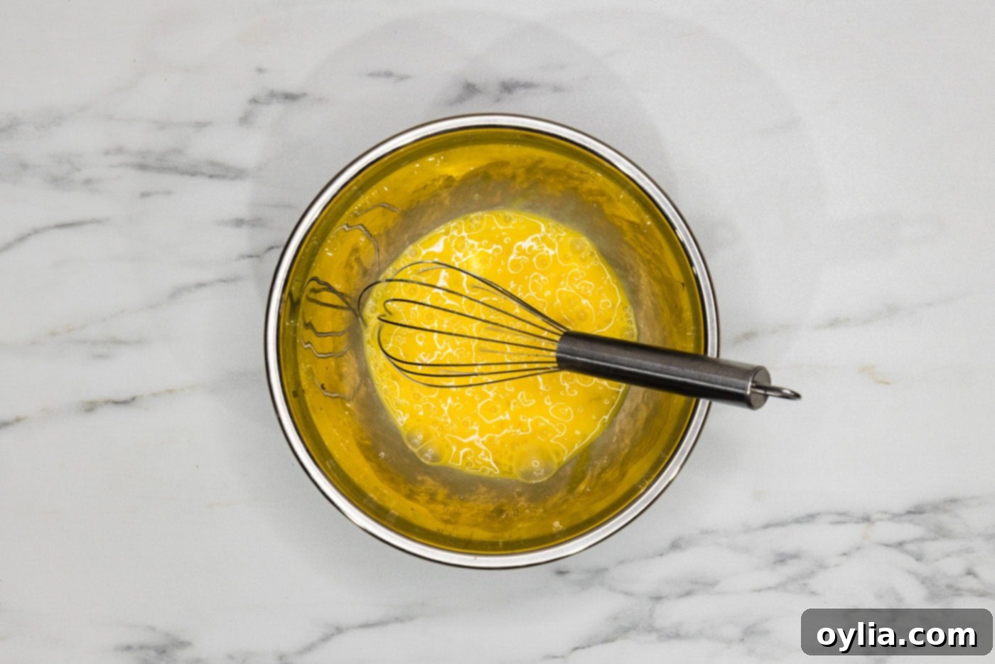 A bowl of whisked egg mixture with a whisk, ready to be added to the sauce