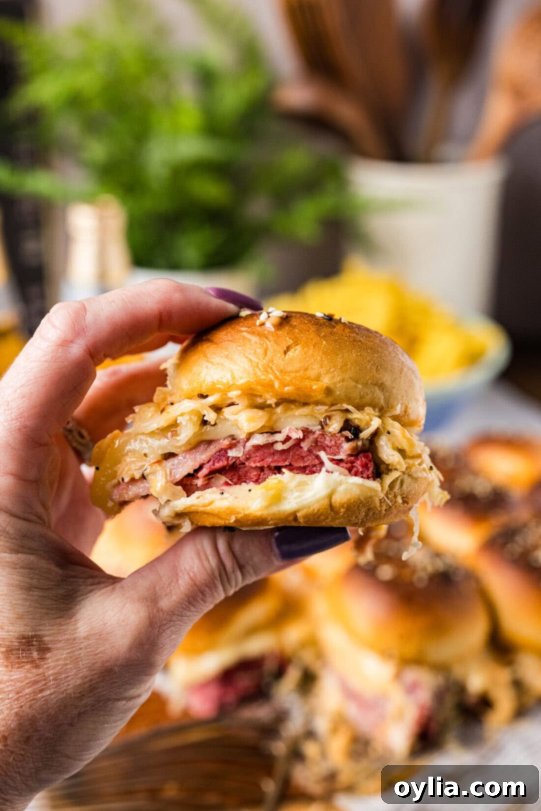 A hand reaching for a golden-brown Reuben Slider from a serving tray