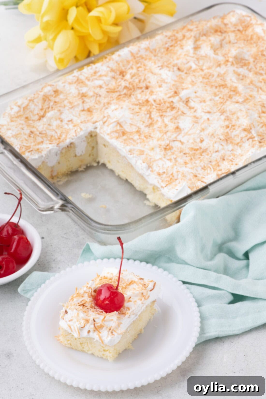 Slice of Coconut Poke Cake on a plate with the rest of the cake in the background