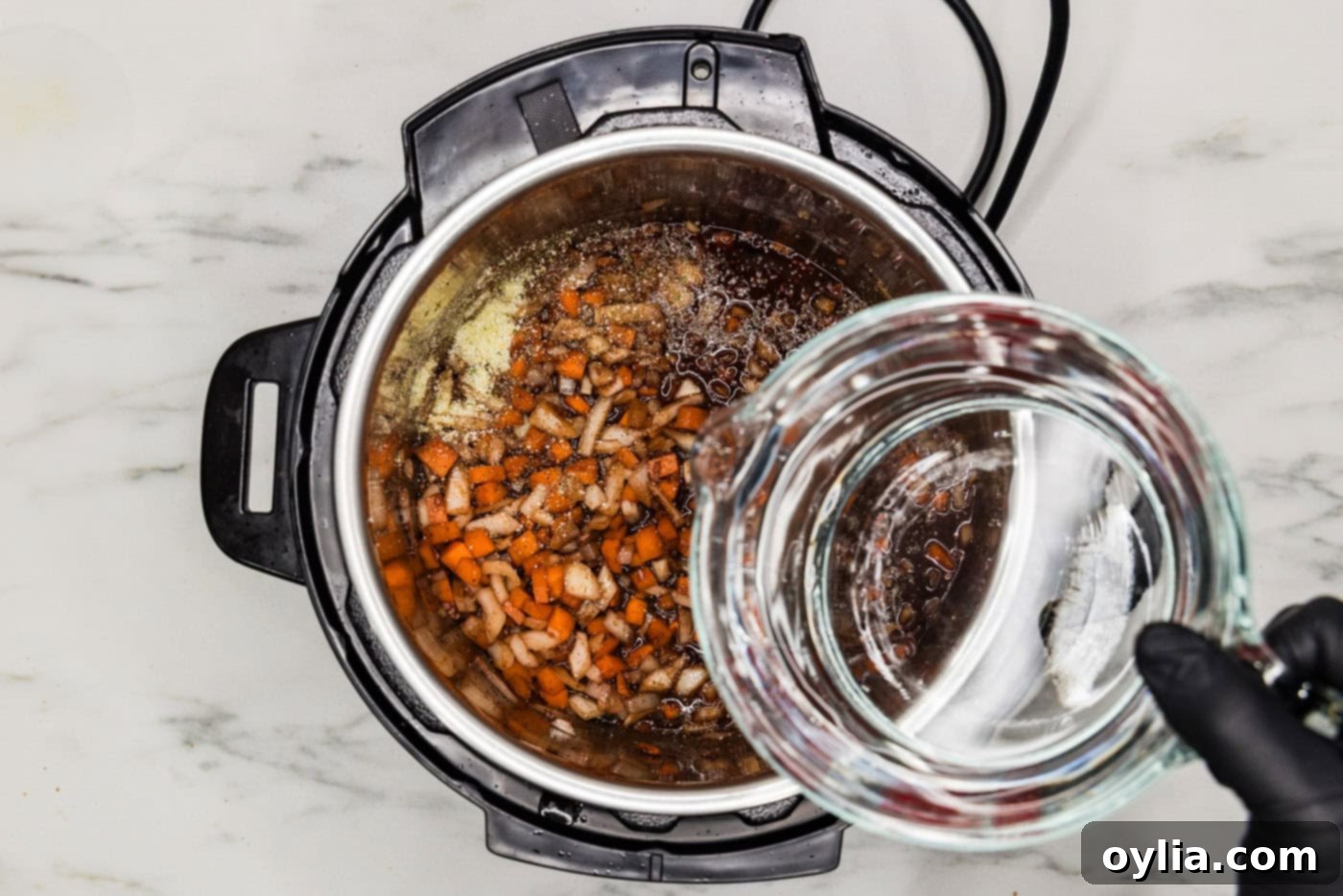 Pouring water into the Instant Pot over beef shanks and vegetables, preparing for pressure cooking.