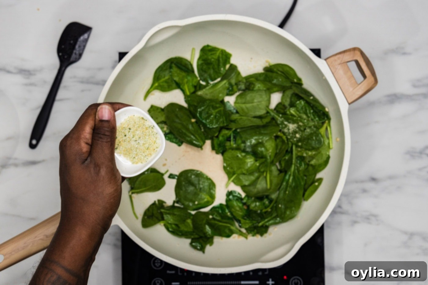 Seasoning fresh spinach and garlic in a skillet with garlic salt, starting the flavorful base for the pesto pasta.