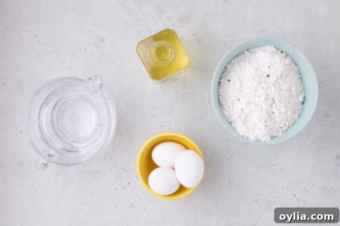 Ingredients laid out for Cake Mix Waffles: a box of funfetti cake mix, eggs, water, and vegetable oil.