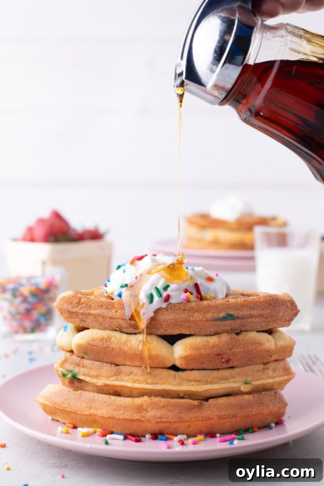 Maple syrup being generously poured over a stack of golden Cake Mix Waffles, garnished with sprinkles.