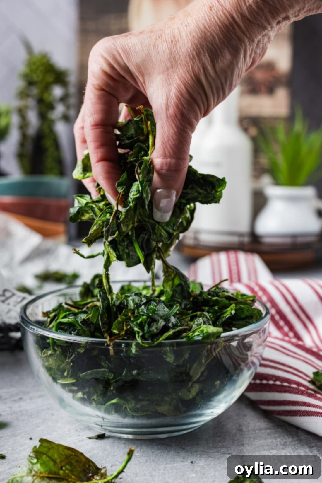 Handful of Crispy Air Fryer Spinach held above a bowl of Crispy Air Fryer Spinach