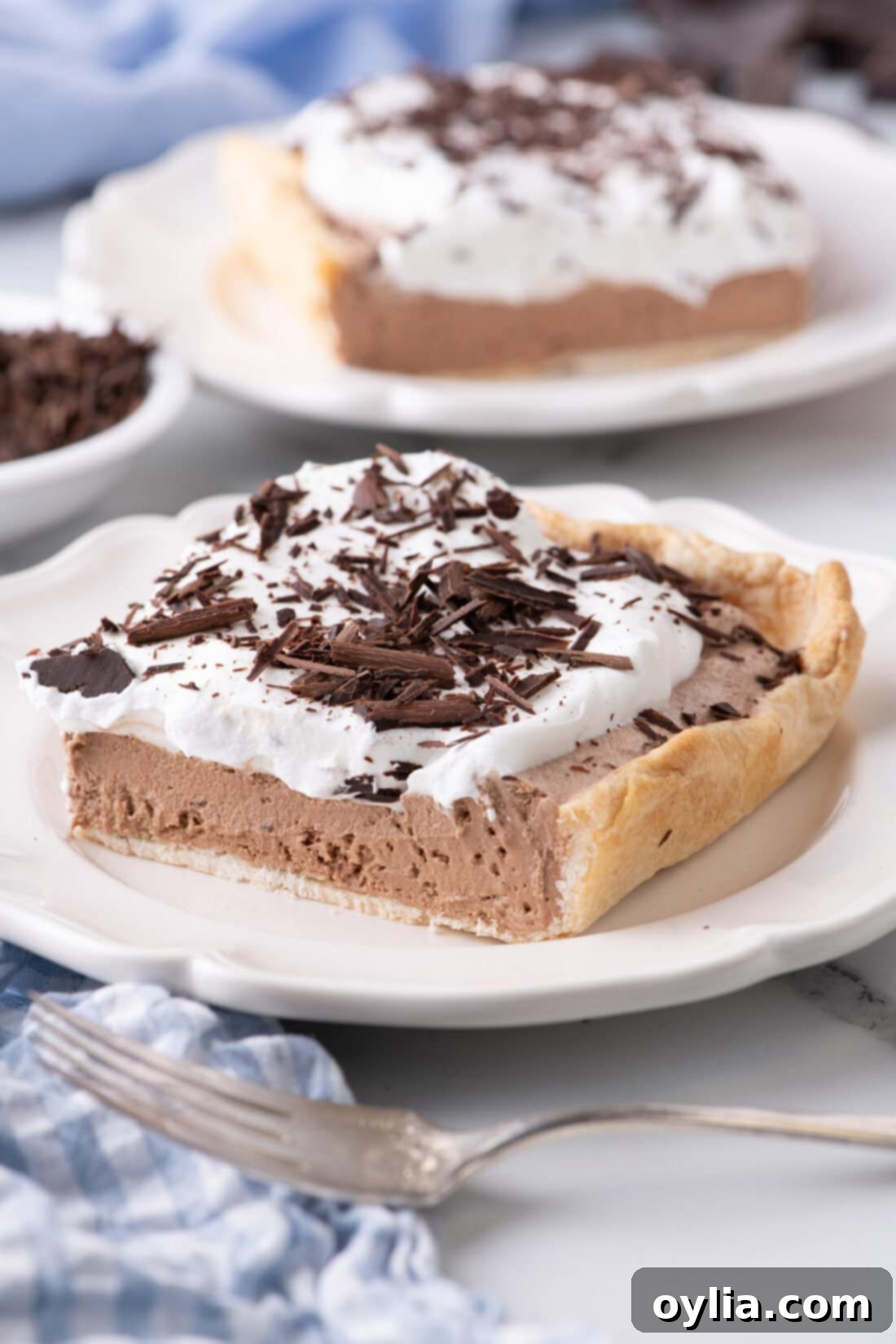 A perfect slice of French Silk Slab Pie on a white plate, showcasing its rich layers of chocolate and whipped cream, topped with chocolate shavings.
