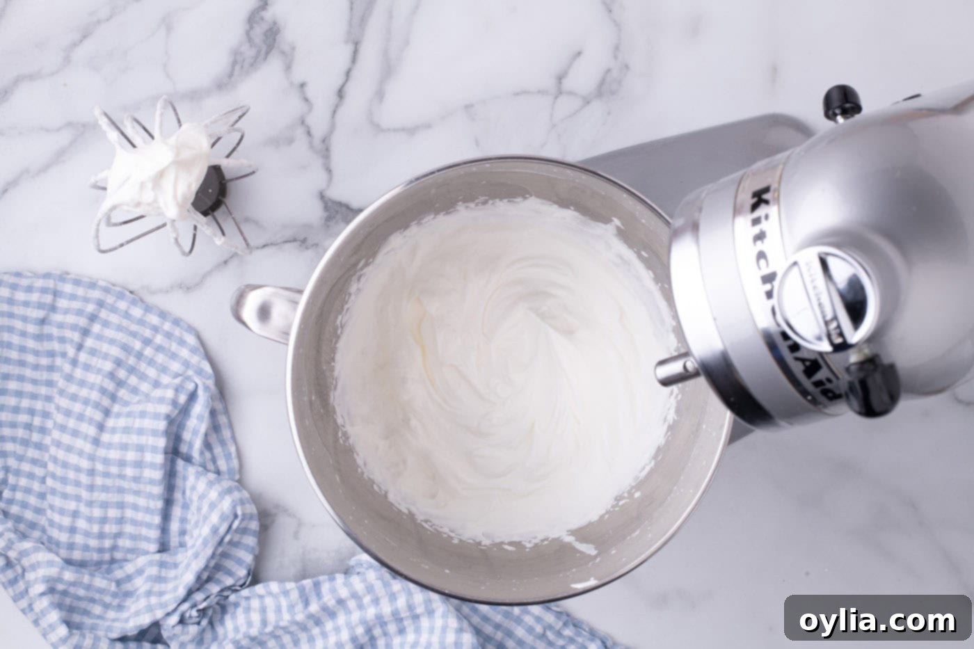 Homemade whipped cream, perfectly fluffy and holding stiff peaks in a stand mixer bowl, ready to be spread over the pie.