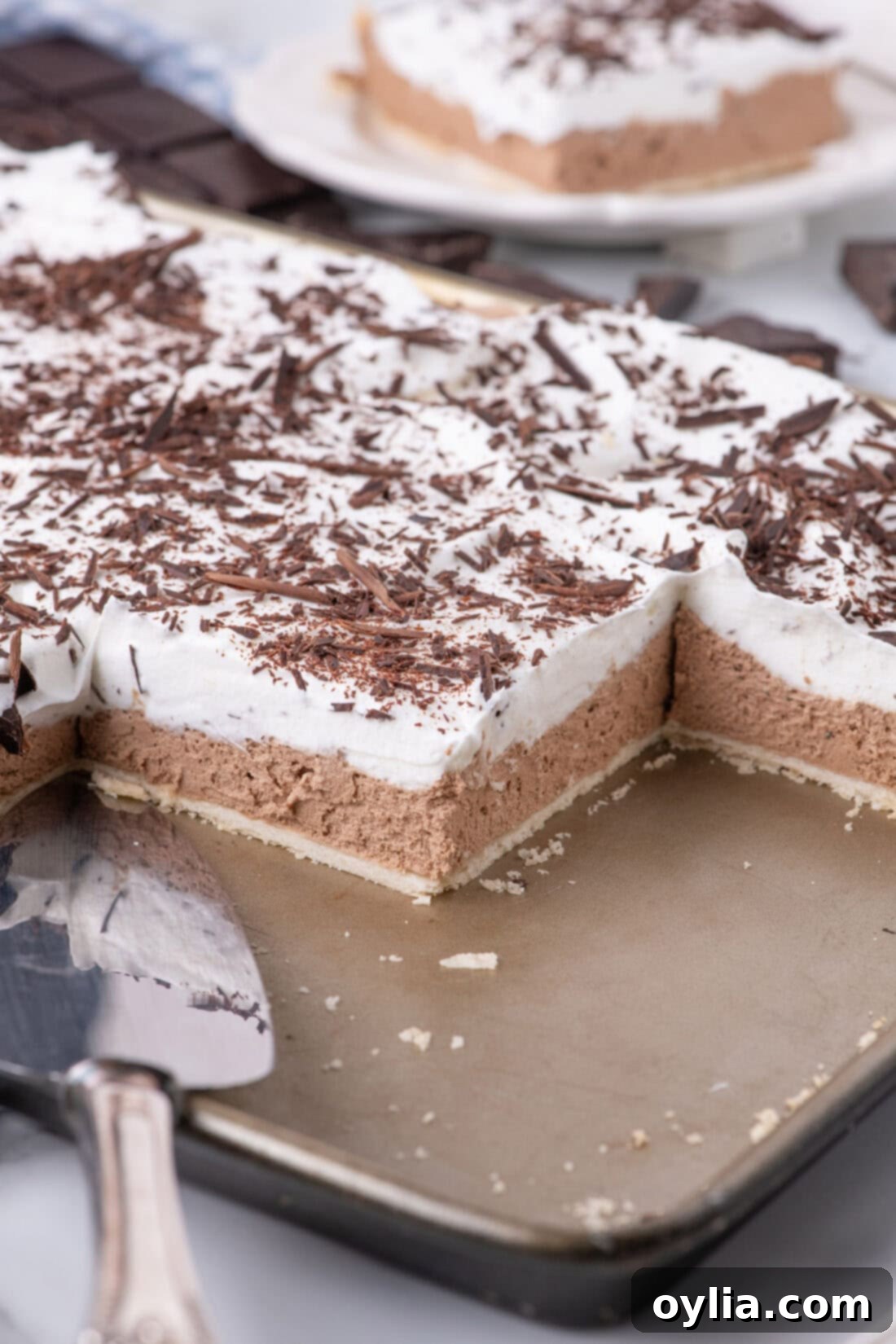 A close-up view of a French Silk Slab Pie with several slices already removed, perfectly showcasing its creamy chocolate filling and luxurious whipped topping.