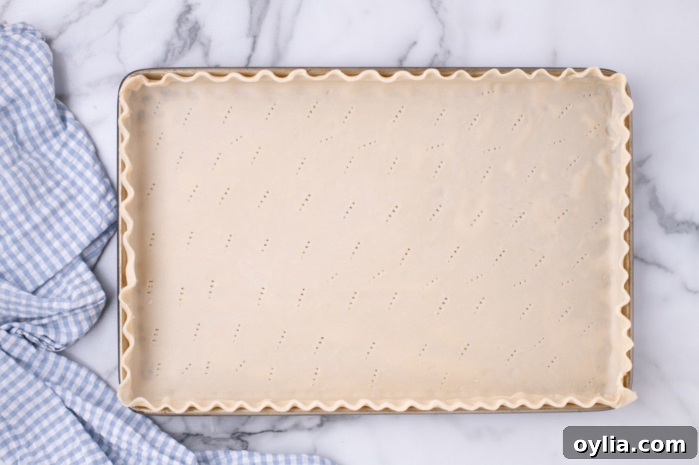 Pie crust with decorative fluted edges, expertly crimped and pricked with a fork, ready for blind baking in a jelly roll pan.