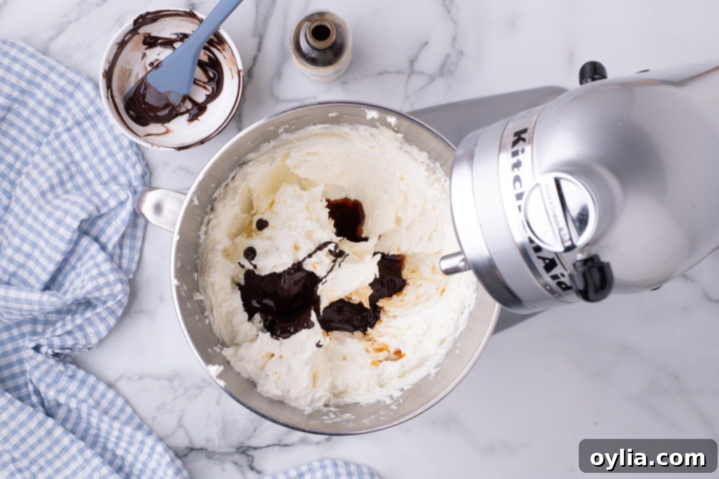 Melted chocolate being gently added and incorporated into the fluffy butter and sugar mixture in a stand mixer.