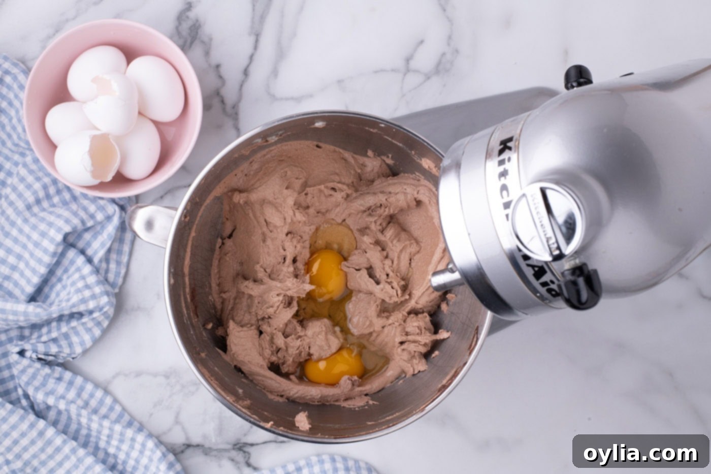 Room temperature eggs being added gradually to the pie filling mixture in a stand mixer, ensuring proper incorporation.