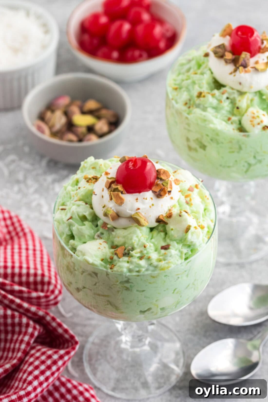 A sundae bowl filled with vibrant green Watergate Salad, topped with a dollop of whipped cream and a single maraschino cherry.