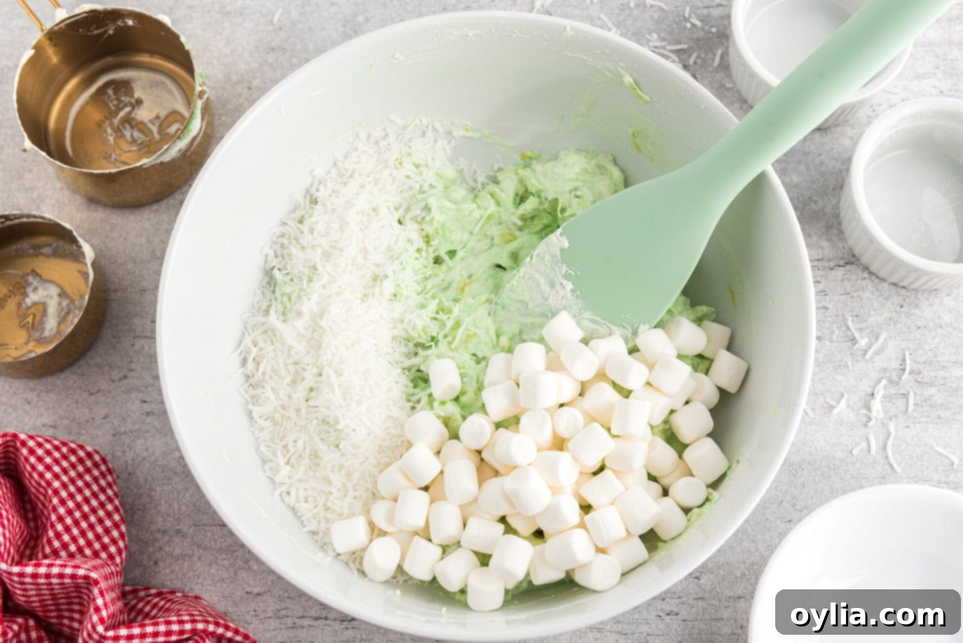 Mini marshmallows and flaked coconut added to the fluffy green pistachio mixture, ready to be combined.