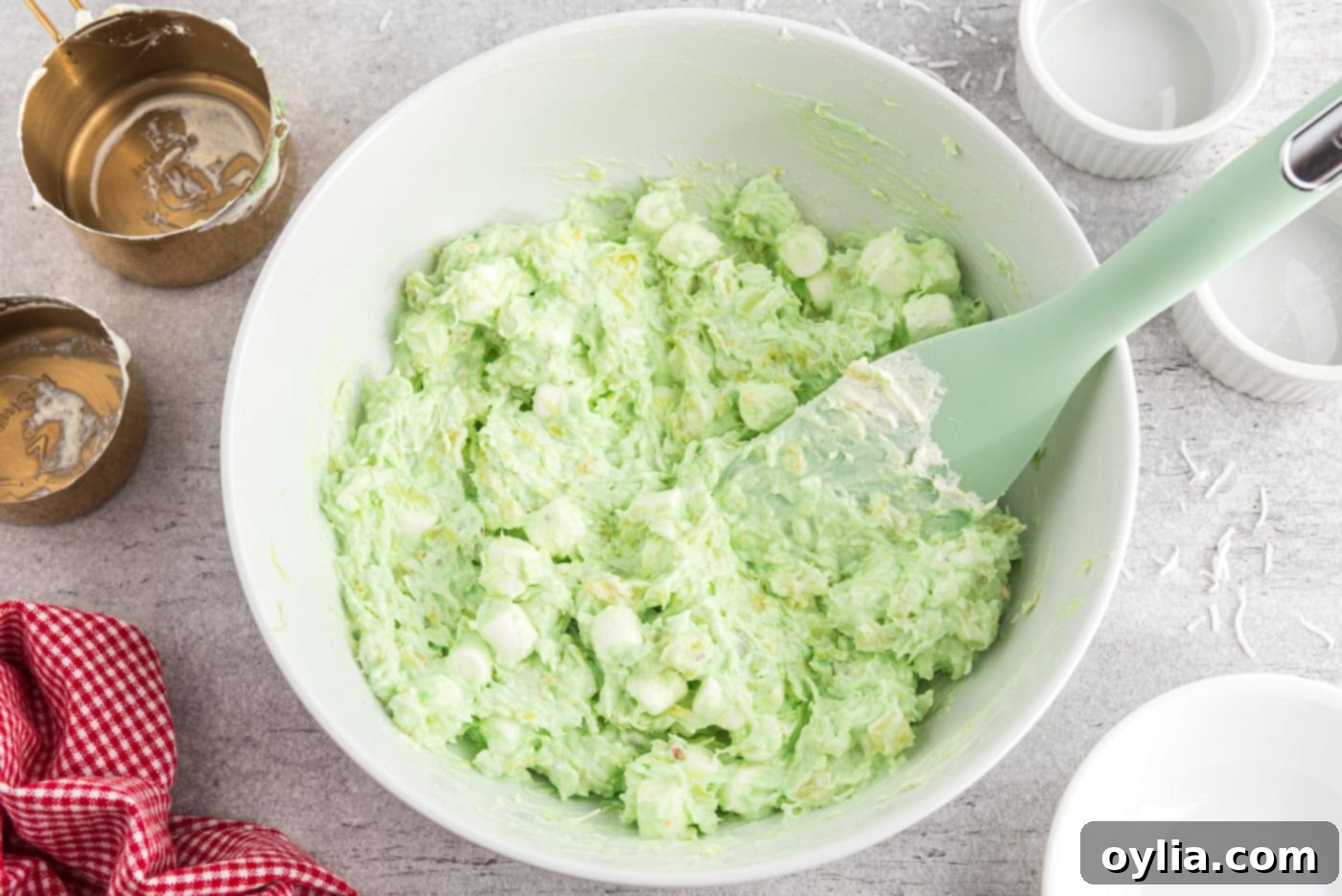 A large bowl of finished Watergate Salad, garnished with a few mini marshmallows, being scooped with a rubber spatula.