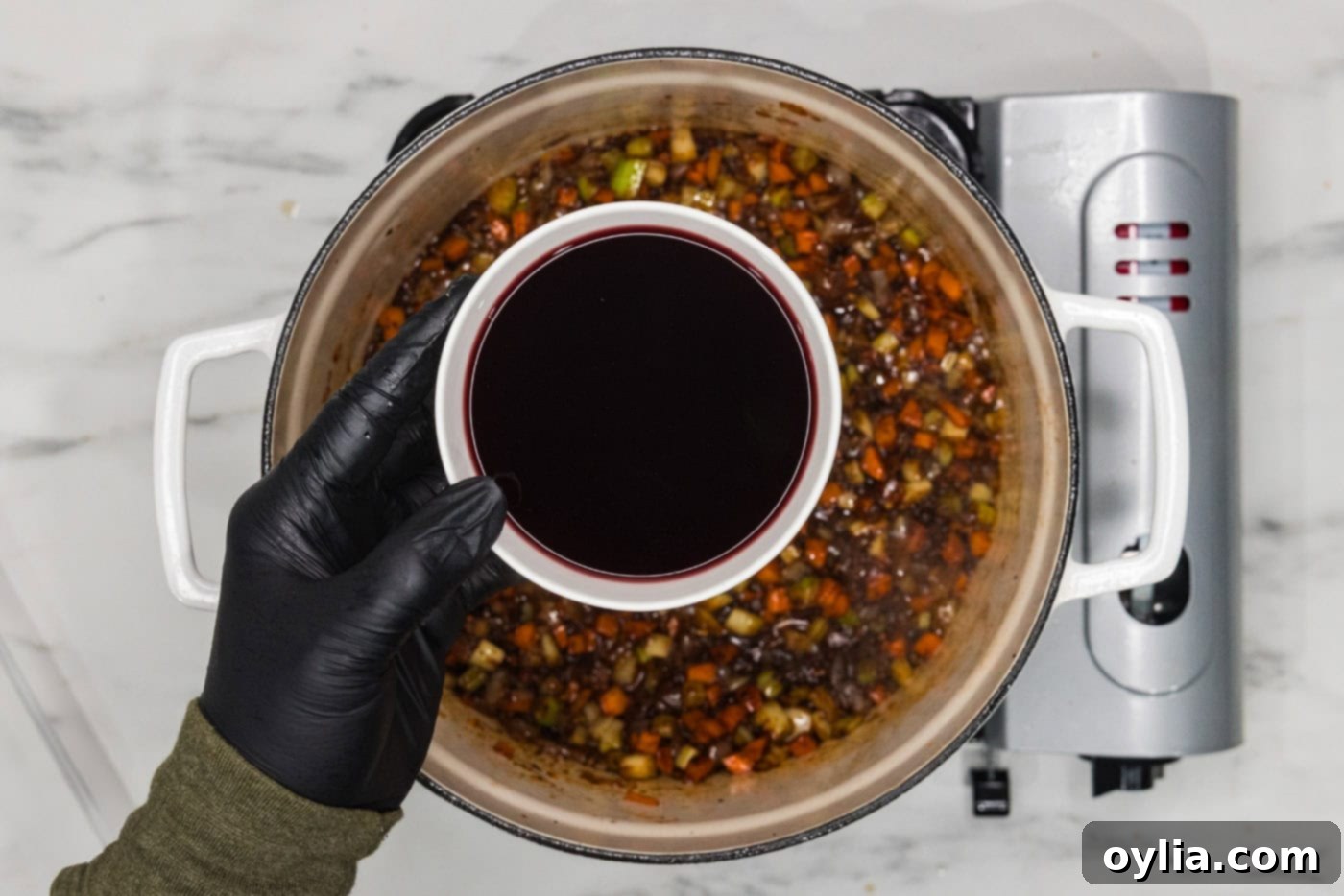 Red wine in a bowl over a dutch oven of vegetables