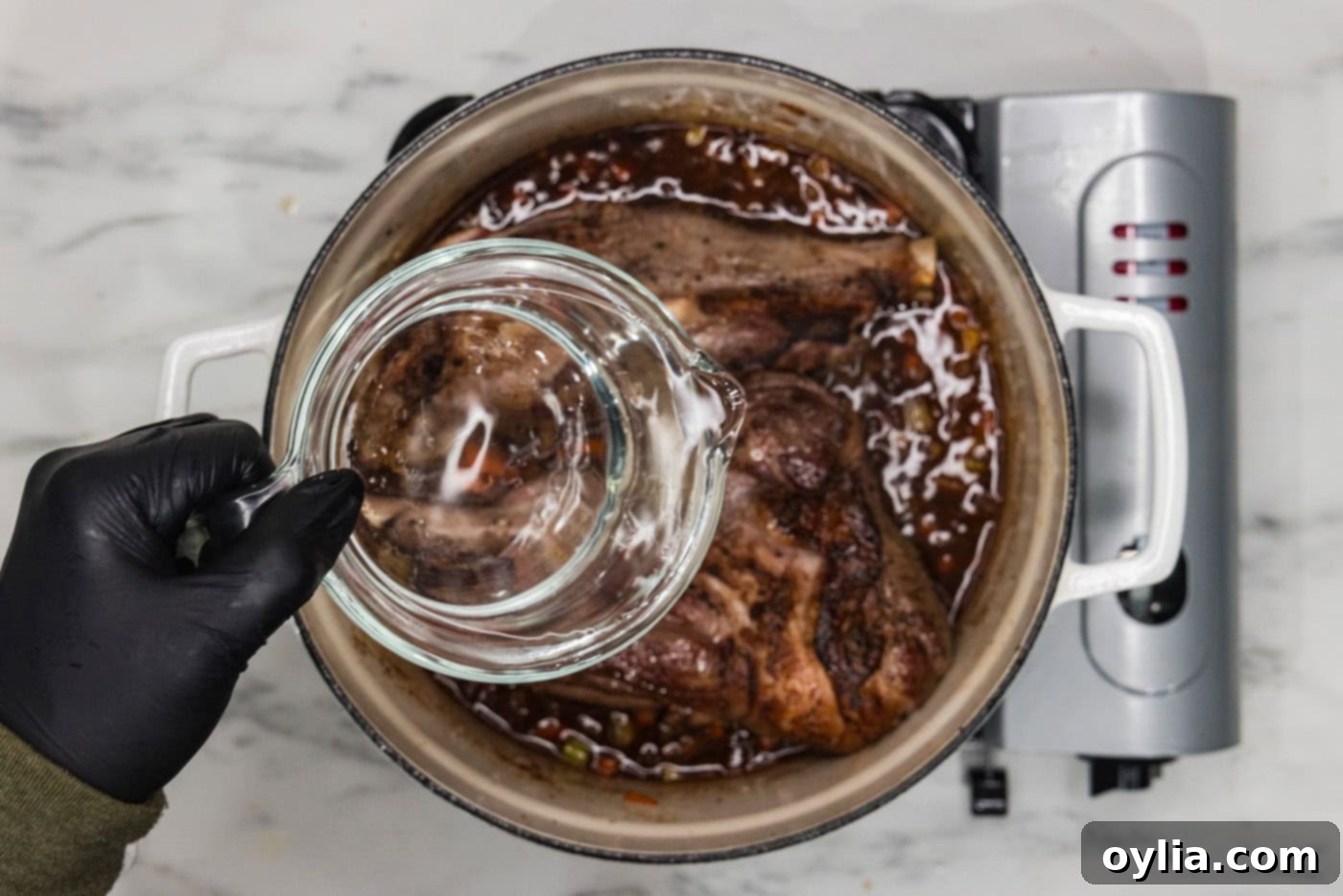 pouring water into dutch oven with braised lamb shanks