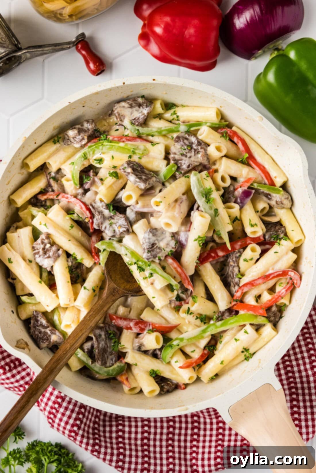 Skillet of Philly Cheesesteak Pasta with a spoon in it, showcasing tender steak, colorful peppers, and creamy cheese sauce.