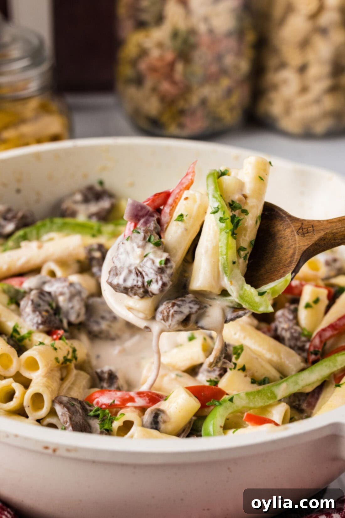 Spoonful of Philly Cheesesteak Pasta held above a skillet, showing the creamy texture and hearty ingredients.