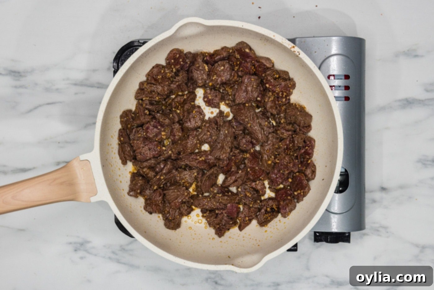 sliced steak and seasonings in a skillet, sizzling and browning.