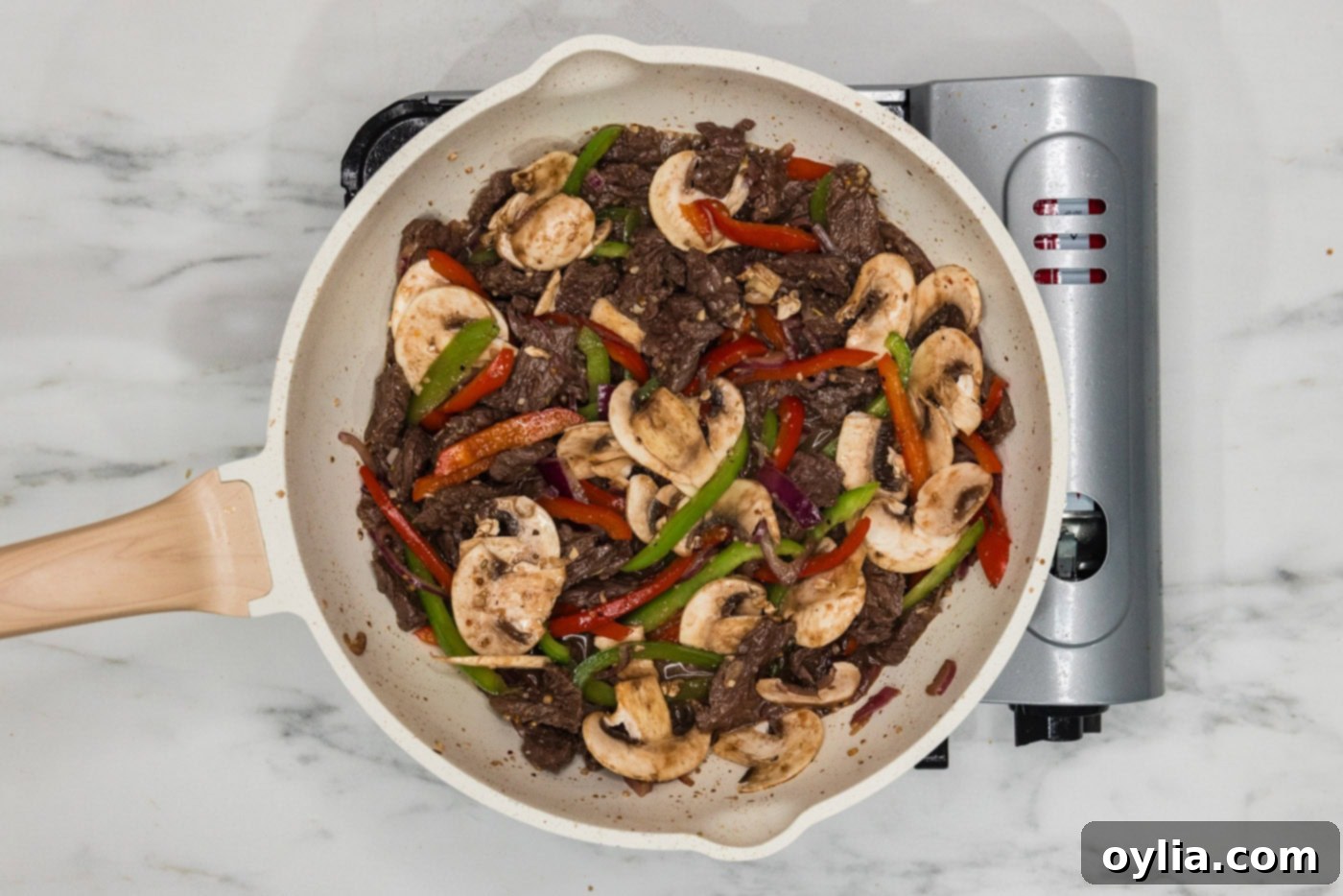 mushrooms, peppers, and onions added to skillet with sliced beef, all cooking together.