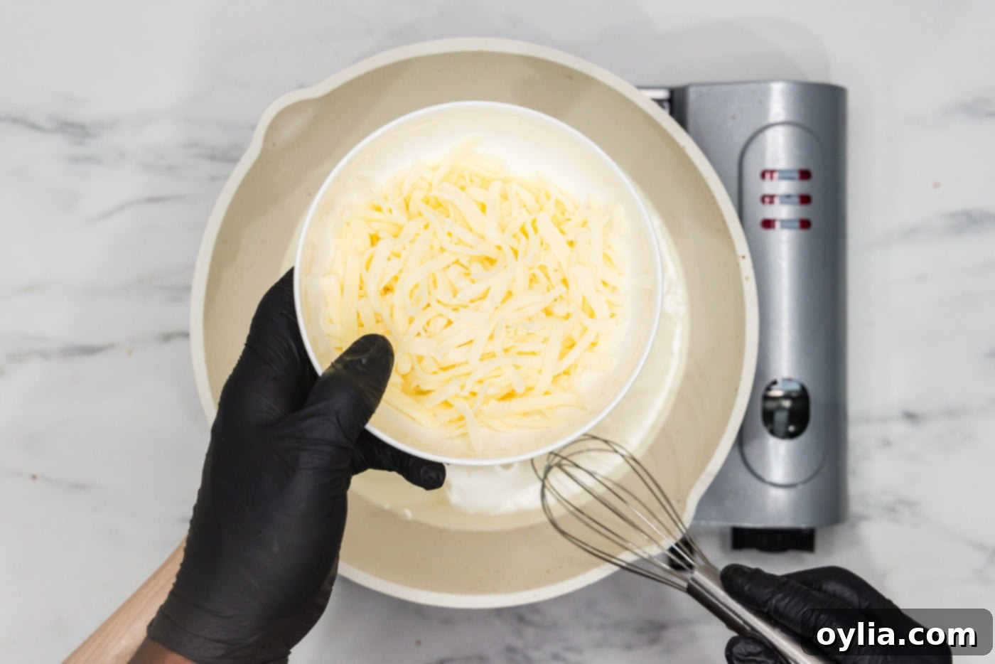hand holding cheese over a skillet of heavy cream, preparing to make cheese sauce.