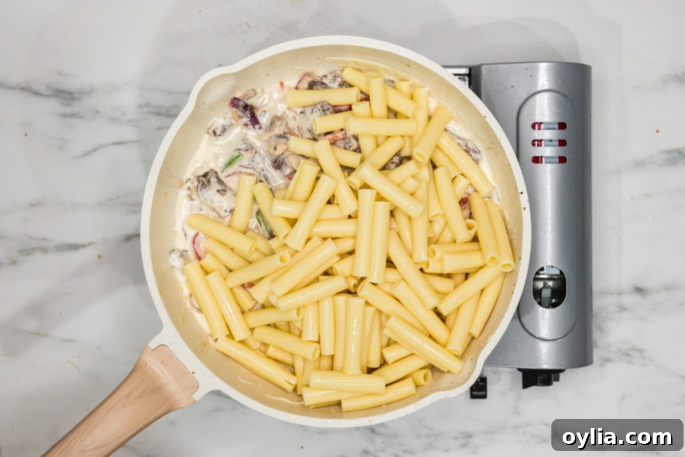 pasta added to skillet with meat, veggies, and cheese sauce, ready to be mixed.