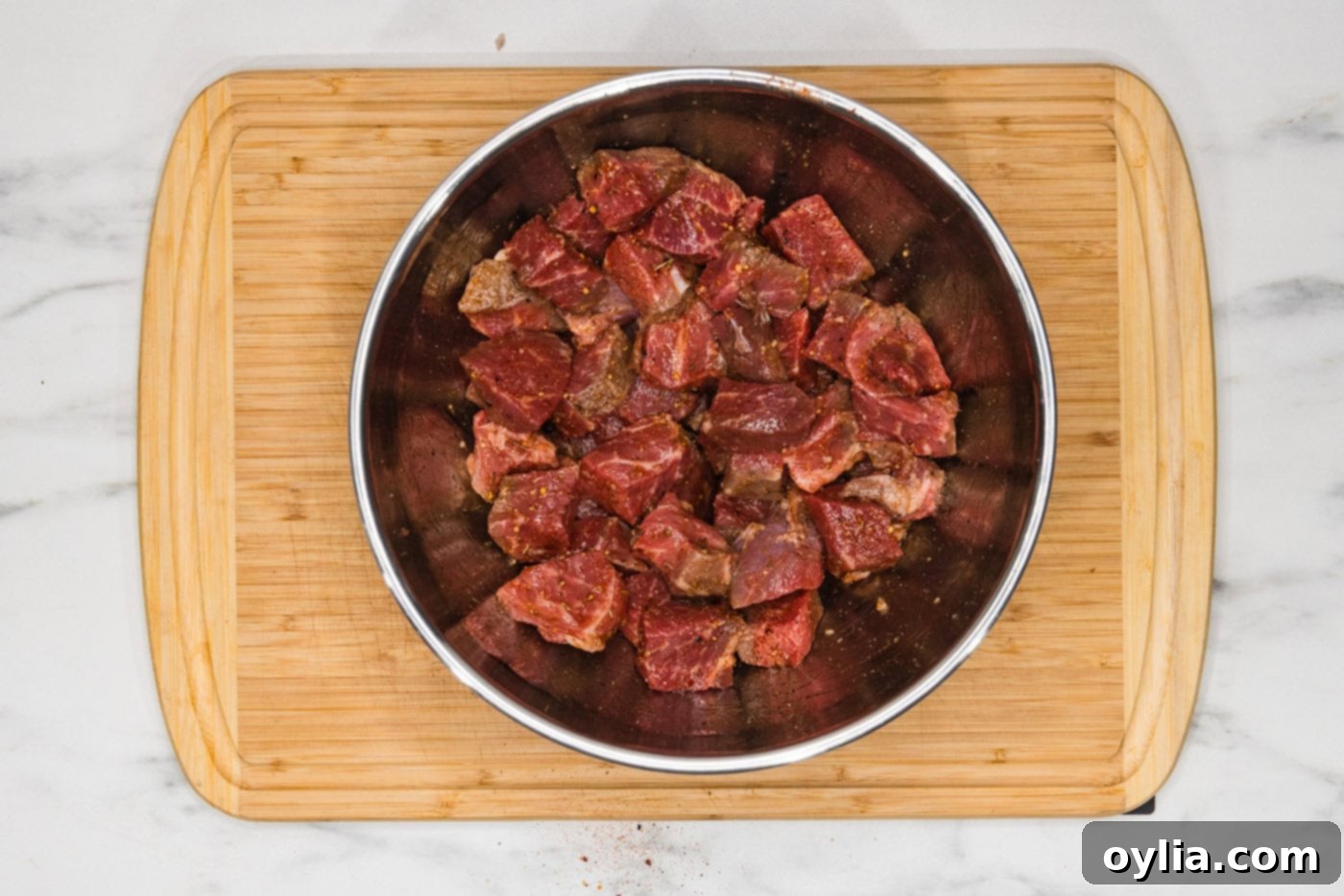 Cubed sirloin steak seasoned with Montreal steak seasoning and olive oil in a mixing bowl, ready for the air fryer.