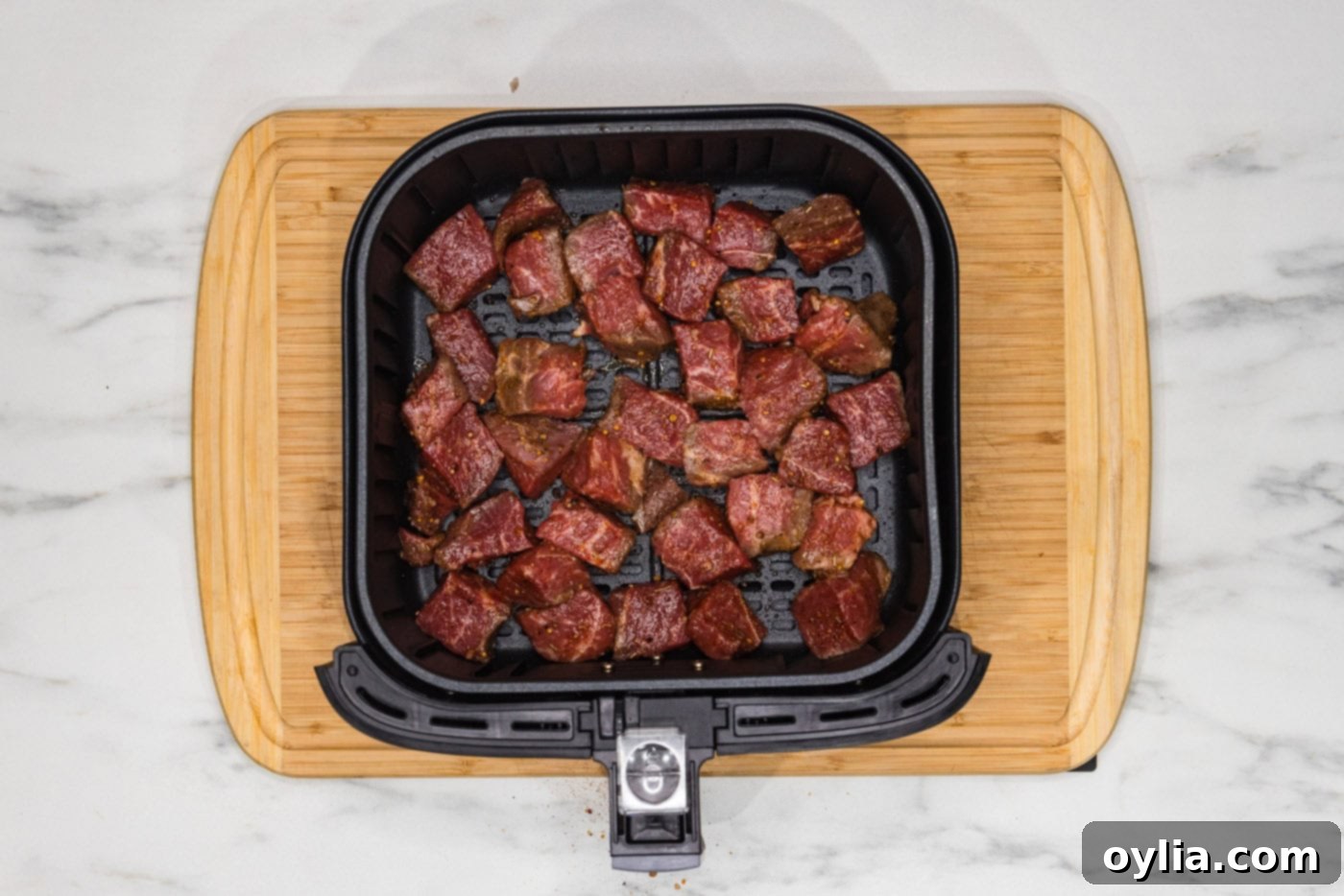 Seasoned steak bites arranged in a single layer inside an air fryer basket, ready for cooking.