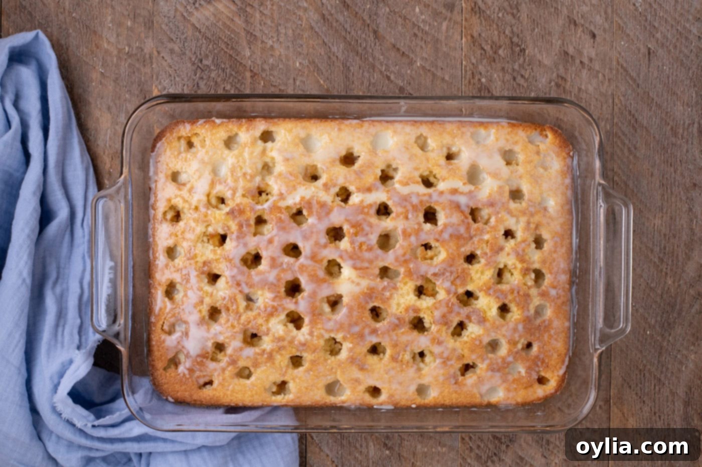 sweetened condensed milk being spread into the poked holes of the warm cake with a spatula
