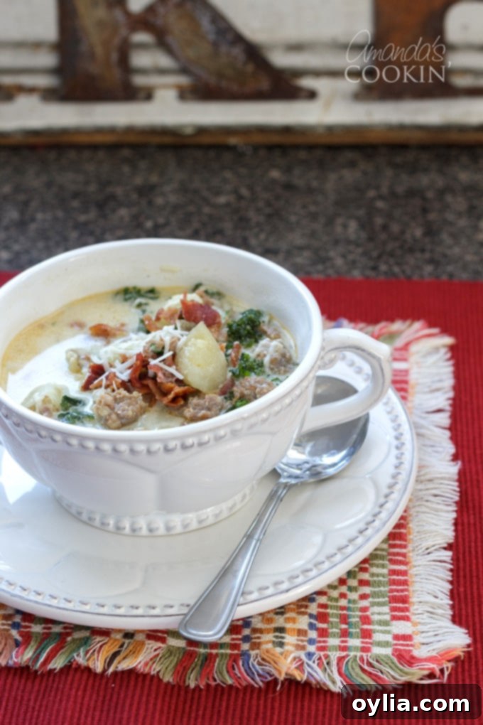 A bowl of Zuppa Toscana soup on a rustic red placemat, garnished with cheese and bacon