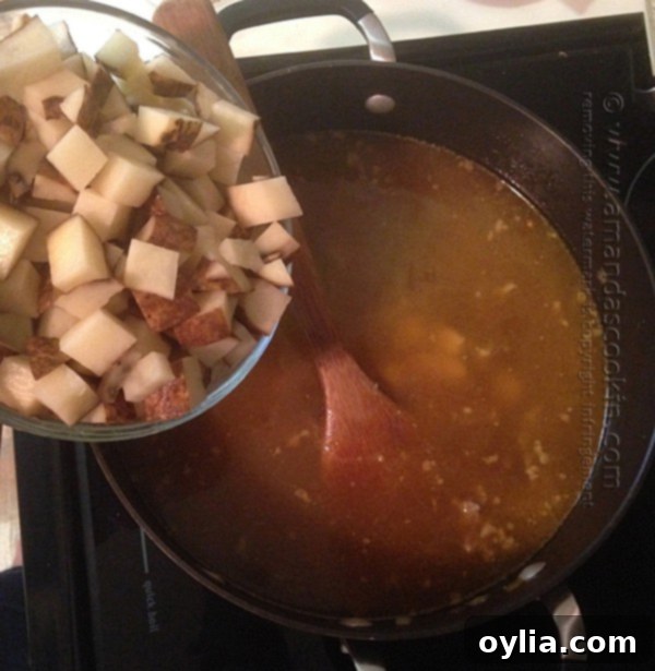 Adding cubed potatoes to the soup pot with chicken broth and sausage