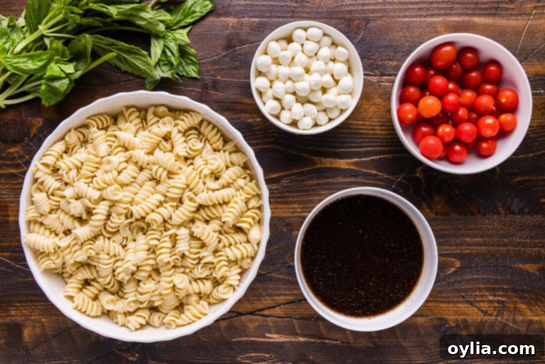 Various fresh ingredients for Caprese Pasta Salad laid out on a wooden cutting board, including rotini pasta, cherry tomatoes, mozzarella pearls, and fresh basil leaves.
