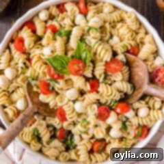 Close up photo of a vibrant Caprese Pasta Salad in a bowl, with two serving spoons, ready to be enjoyed.