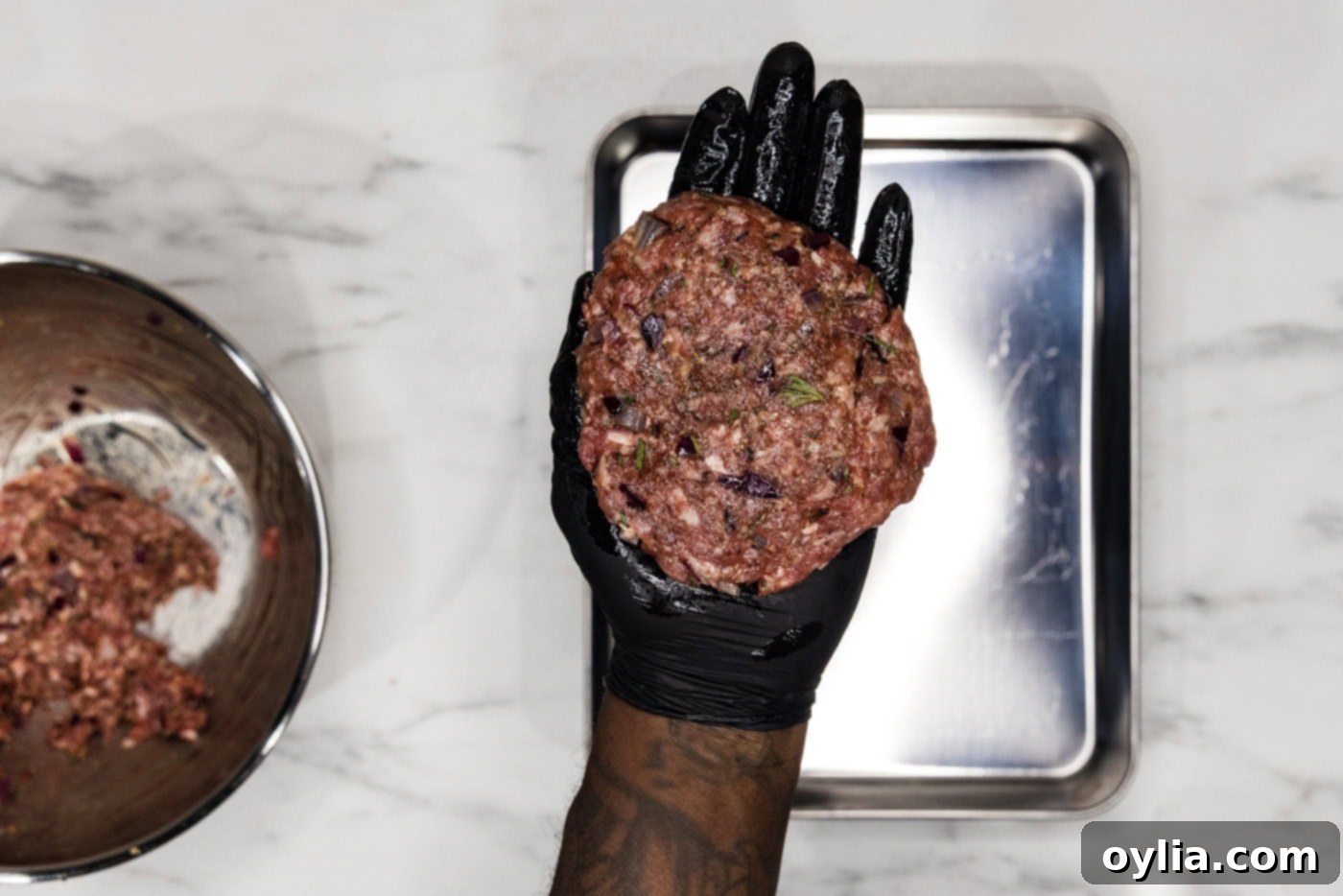 gloved hand holding a lamb burger patty