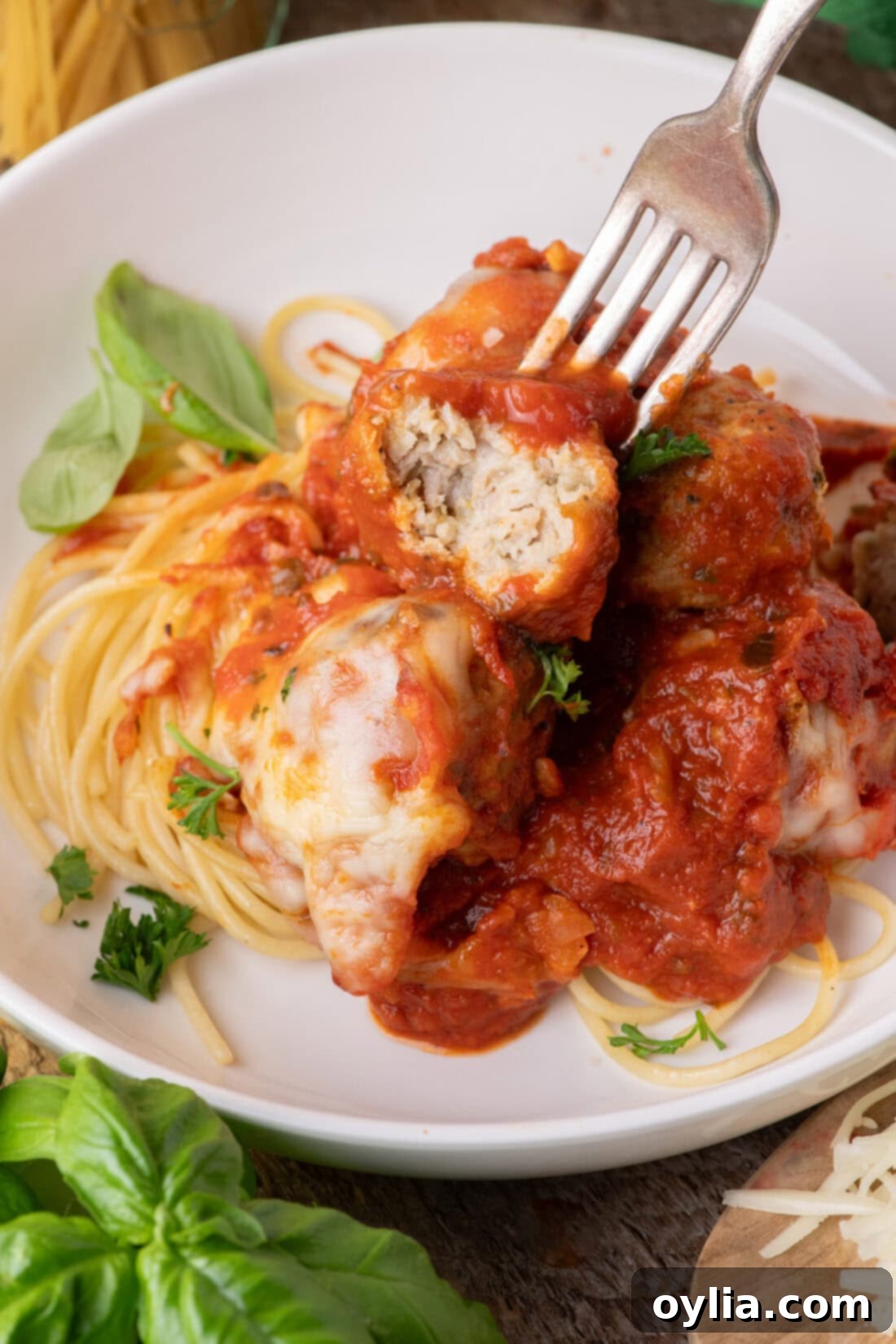 Cheesy Chicken Parm Meatballs 3 Fork holding half of a Chicken Parmesan Meatball over spaghetti and meatballs