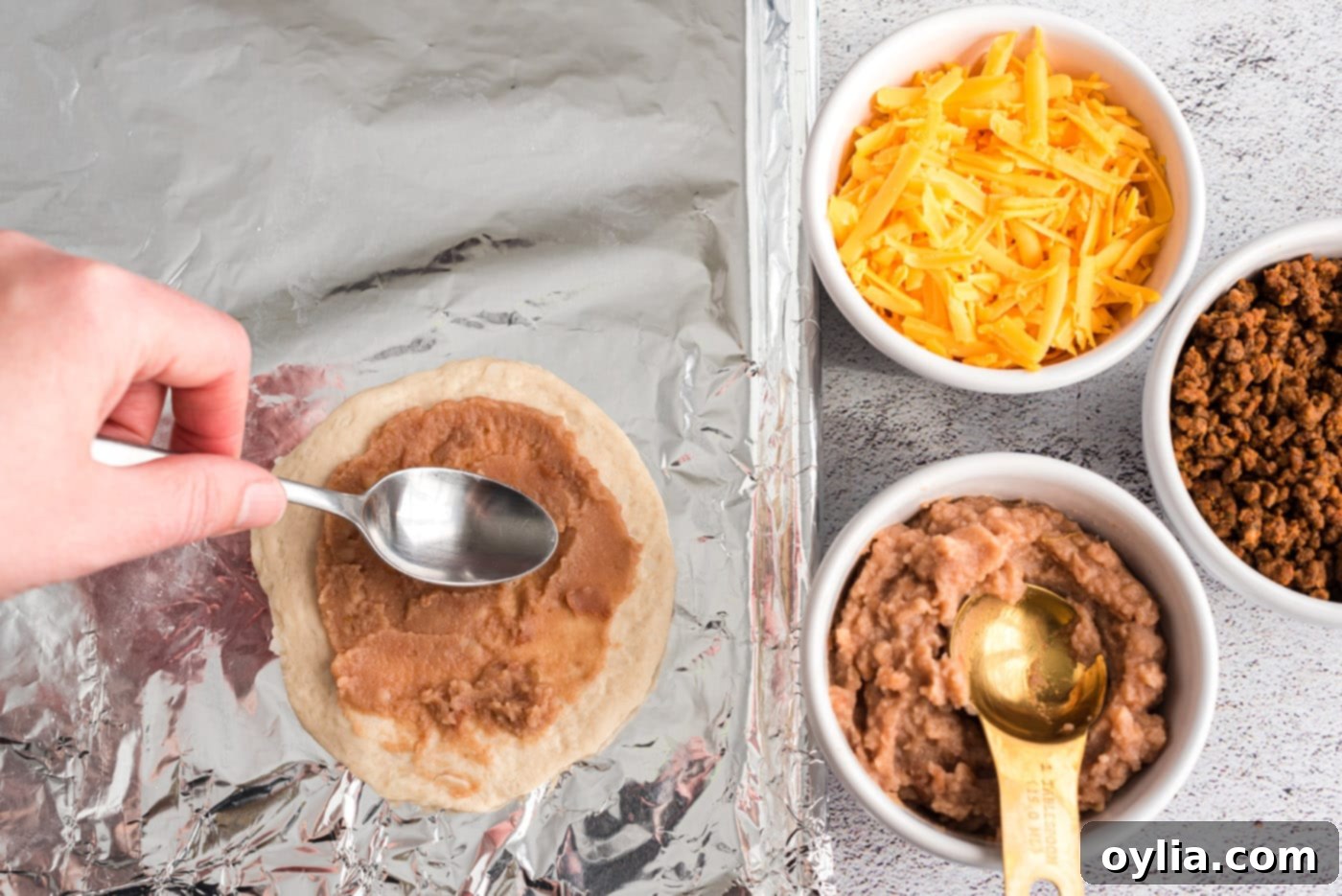 spreading refried beans on biscuit dough for taco empanadas