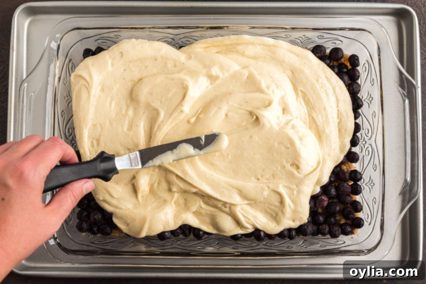 Spreading cake batter gently over the blueberry and brown sugar mixture in the baking dish for an even layer