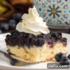 Square of Easy Blueberry Upside Down Cake on a plate topped with whipped cream, showing the beautiful berry topping.