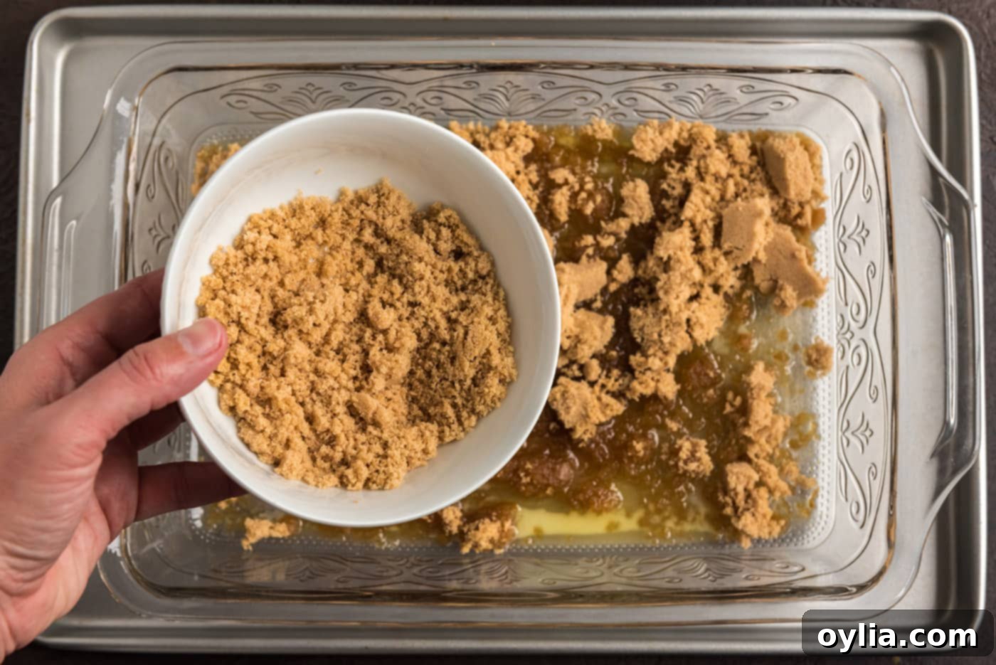 Sprinkling brown sugar over melted butter in a baking dish, preparing the base for the blueberry topping
