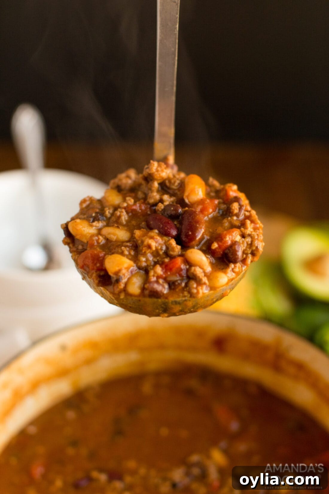A ladle scooping a generous portion of hearty 3 bean chili from a pot, showcasing the rich color, visible ground beef, and various beans.