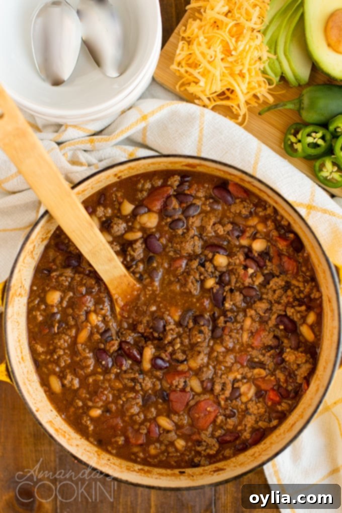 An overhead view of a large Dutch oven filled with simmering three bean chili, steam gently rising, ready to be served.